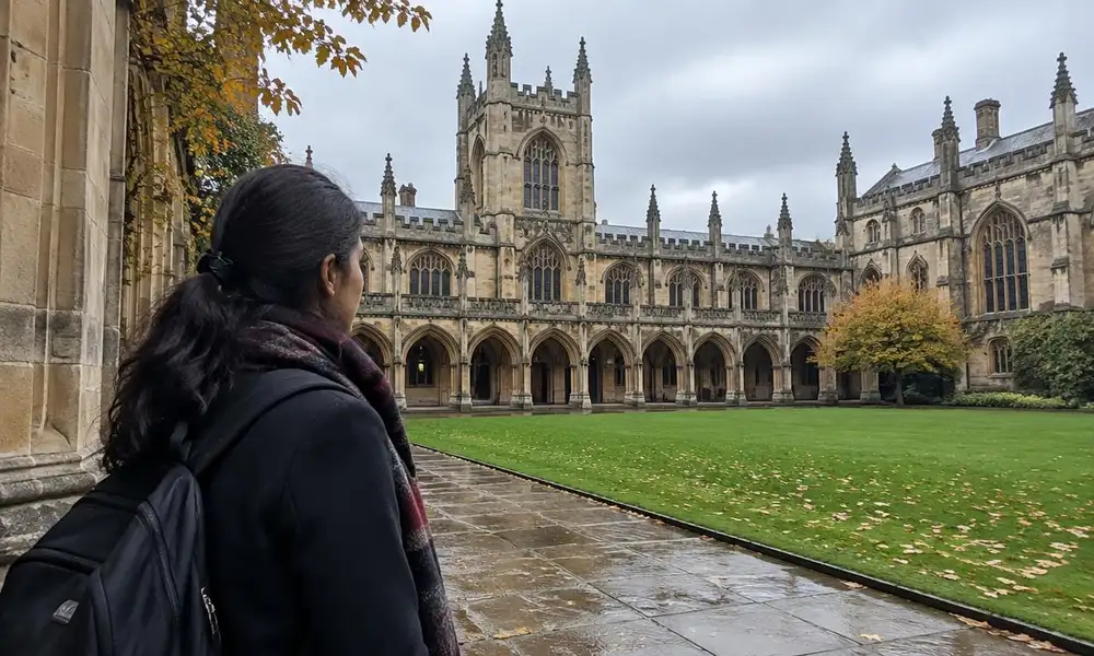 Pakistani student looking across a Gothic stone quadrangle at a UK university